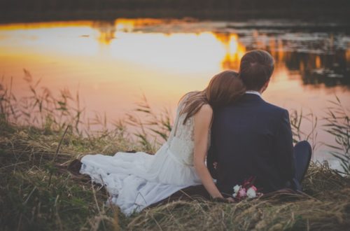Wedding Couple Sitting In Front Of Water At Sunset